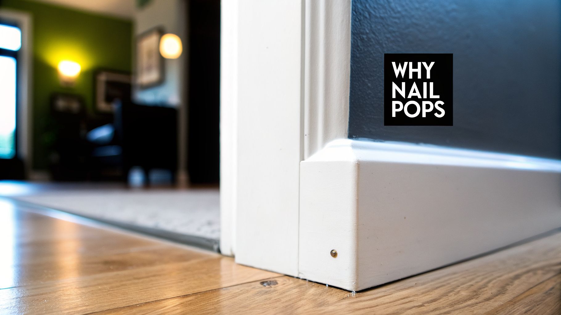Close-up of a white baseboard with a visible nail pop next to a wooden floor.