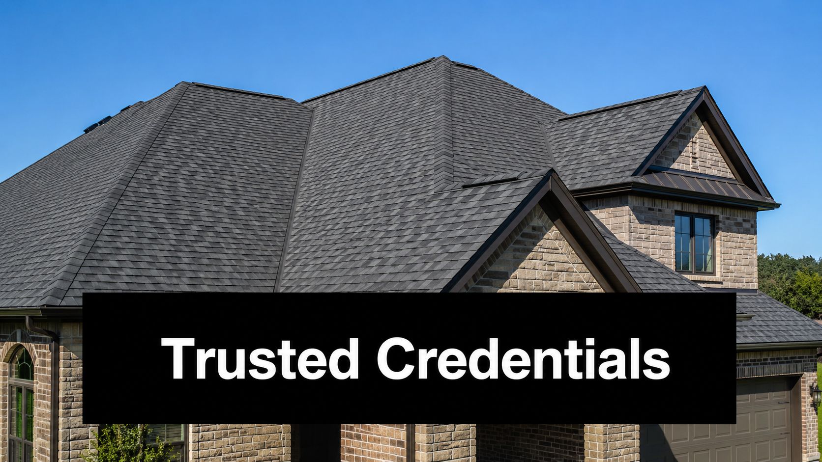 A luxurious custom stone residential house exterior featuring a dark grey shingled roof under a clear sky.